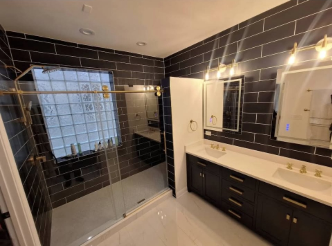 Bathroom with glass shower, double vanity, backlit mirrors and black subway tile